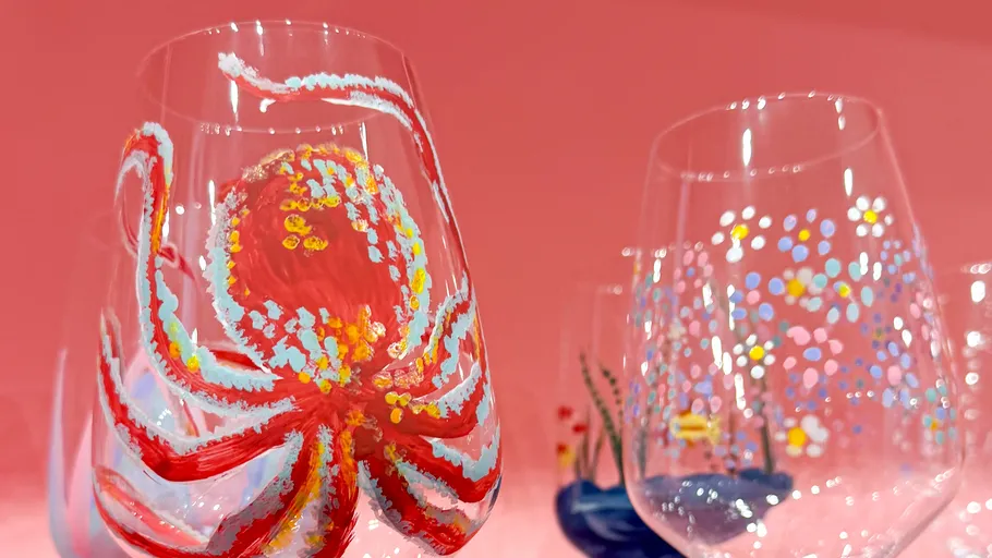 Bemalte Weingläser mit bunten Designs, rosa Hintergrund.