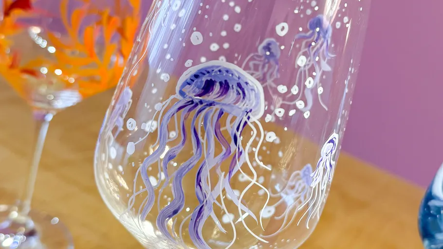 Glass with painted jellyfish on wooden table.