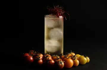 Hoher Cocktail mit Eis, umgeben von Tomaten.