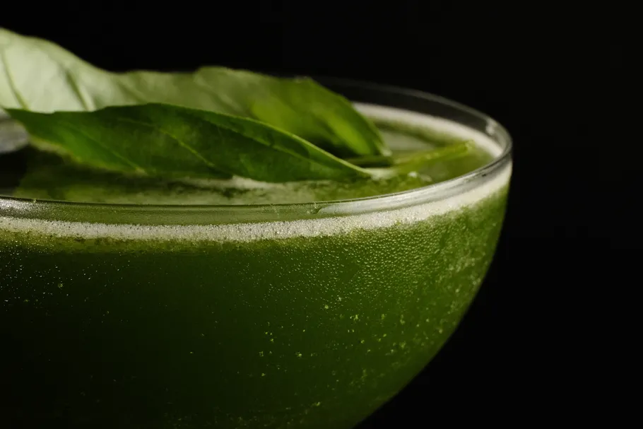 Grüner Cocktail mit Basilikumblättern obendrauf.