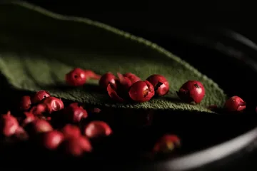 Rote Pfefferkörner auf grünem Blatt, dunkler Hintergrund.