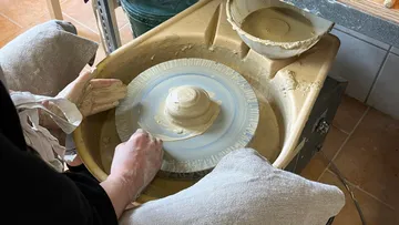 Hands shaping clay on a pottery wheel.