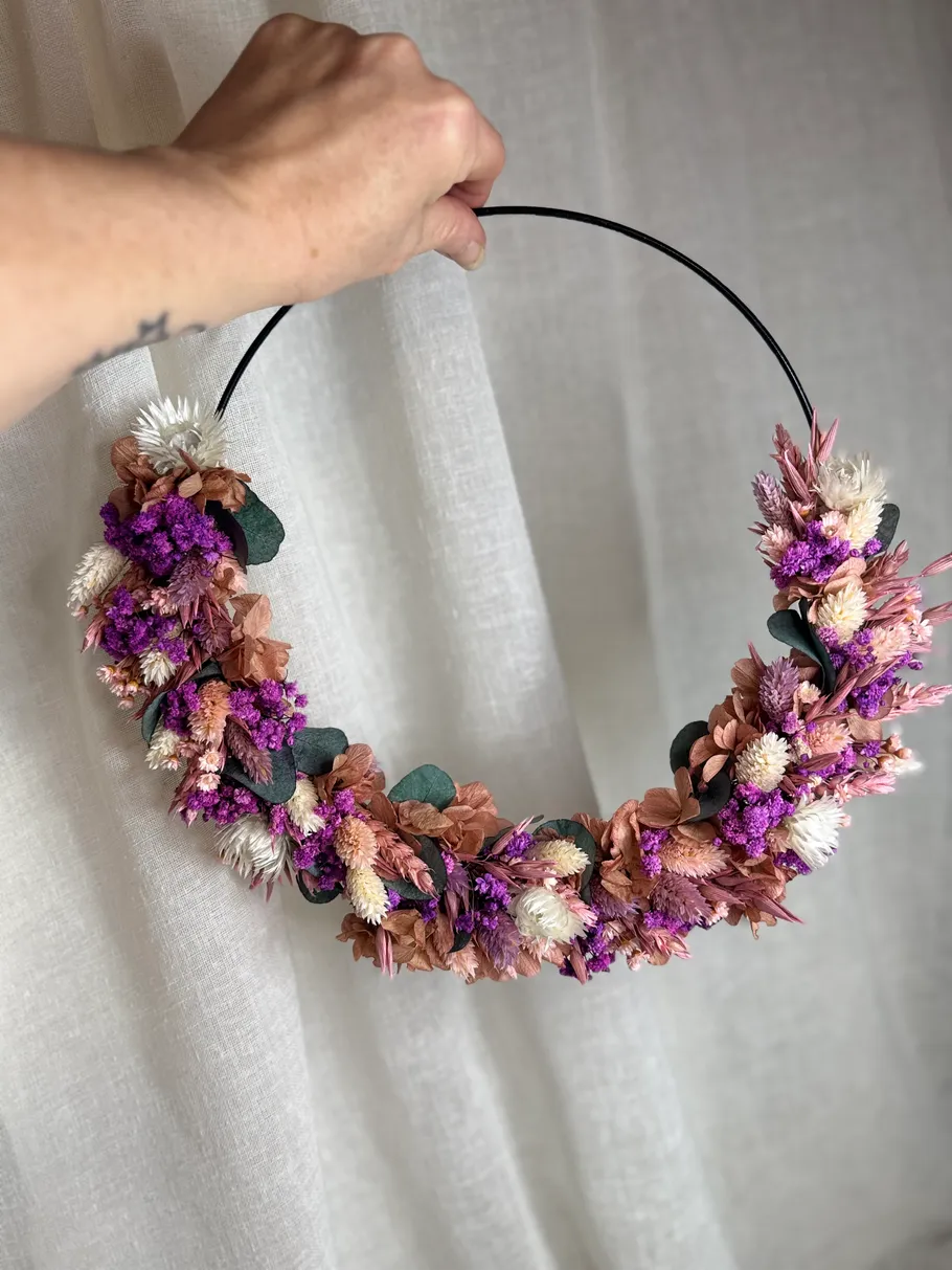 Hand holding colorful floral wreath against curtain.
