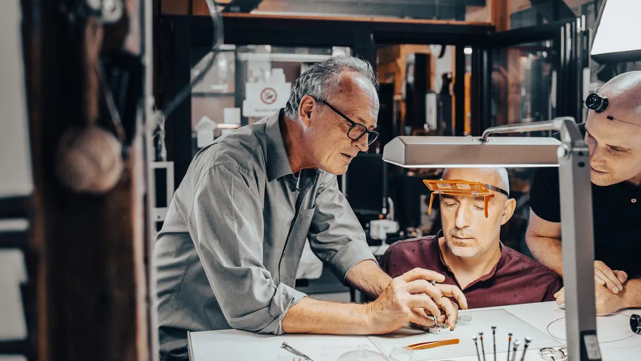 Three men working on watch assembly indoors.