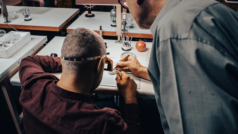 Two people inspecting watch parts at desk.