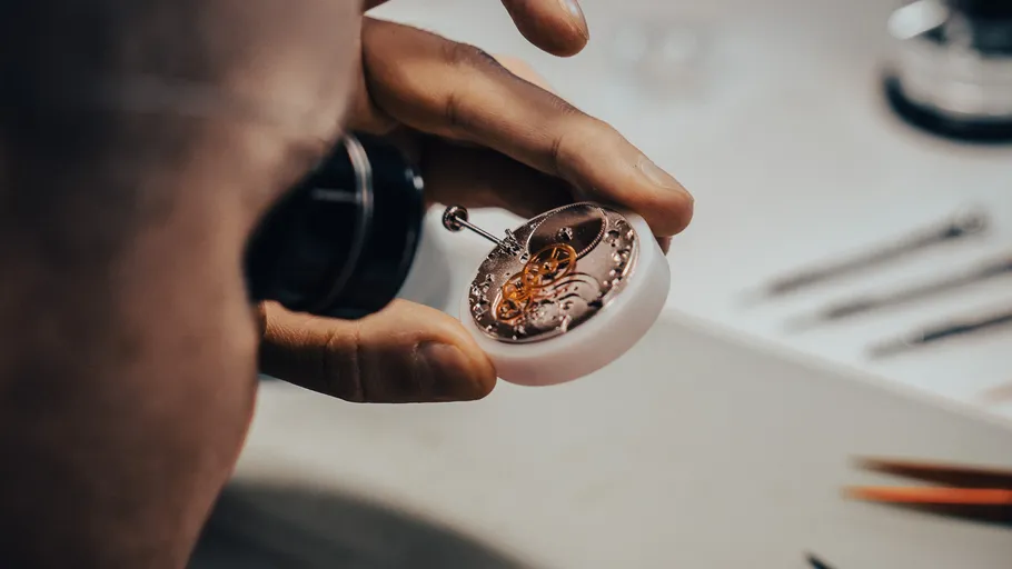 Person repairing watch mechanism on table.