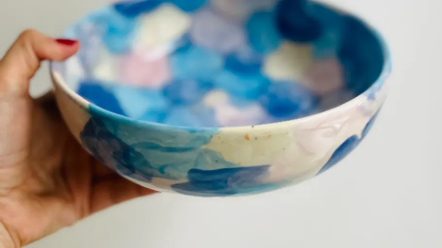 Hand holds colorful ceramic bowl up close.
