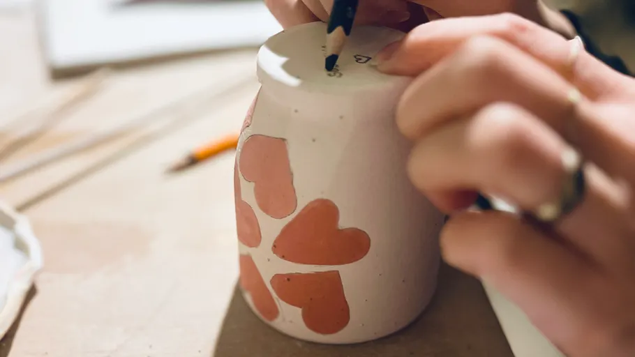 Hände zeichnen auf einem herzgemusterten Becher.