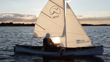 Mann segelt kleines Boot auf See bei Sonnenuntergang.