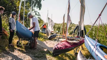Menschen bereiten Segelboote am grasigen Ufer vor.