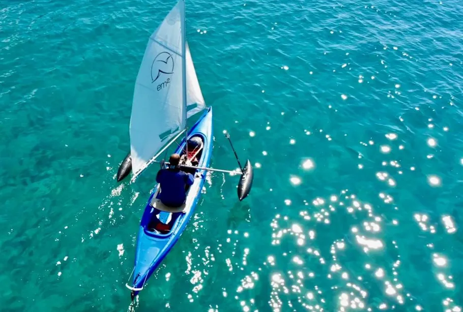 Person kayaking with sail on clear blue water.
