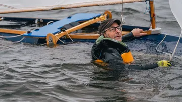 Mann im Wasser hält gekentertes Boot.
