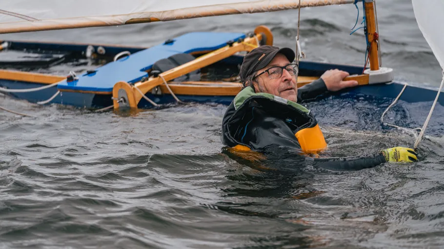 Man in water holding capsized boat.