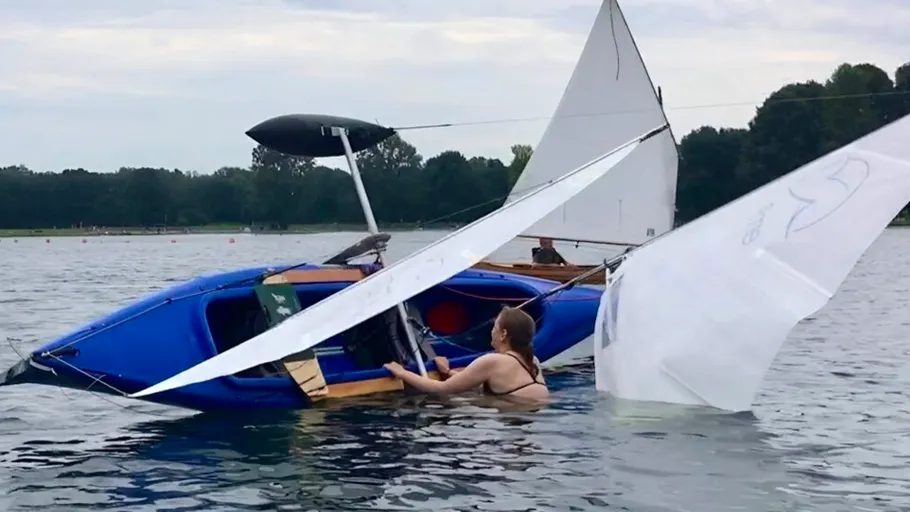 Sailboat capsized with person in water.