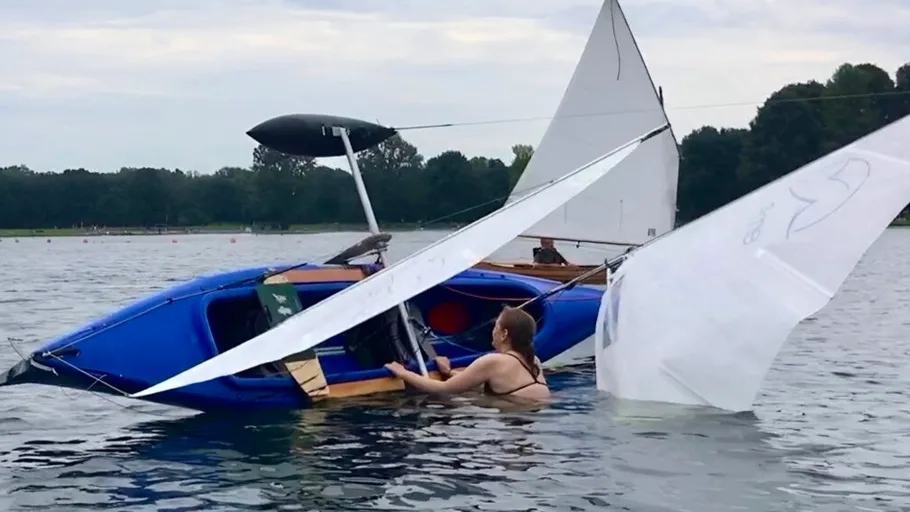 Woman rescuing capsized sailboat on calm lake.