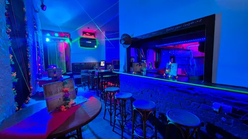 Neon-lit bar interior with stools and tables.