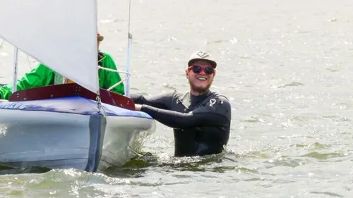 Mann im Wasser schiebt Segelboot vorwärts.