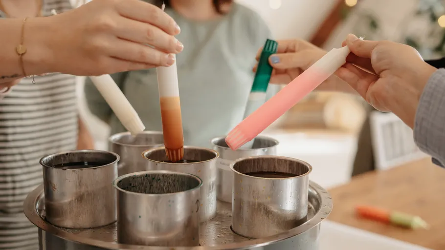 Hands dipping candles in colorful wax.