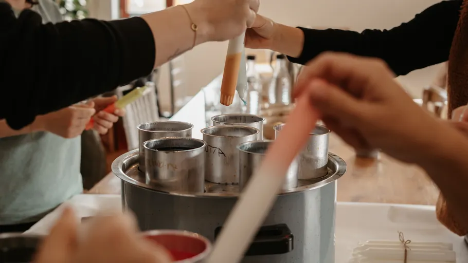 Hands dipping candles in wax molds.