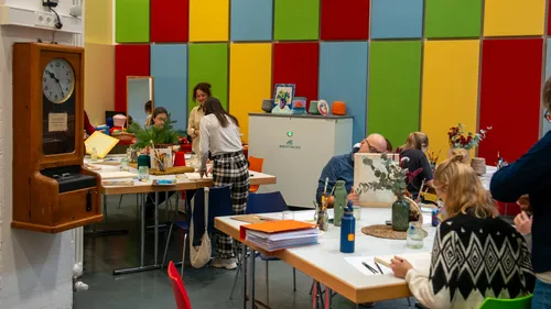 Menschen an Tischen in buntem Kunstworkshop.