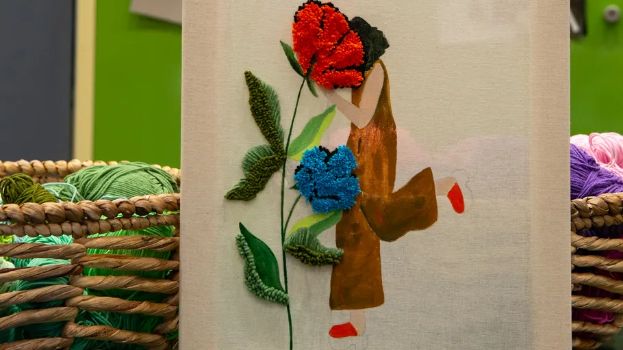 Stickkunst mit Blumen und Figur auf Stoff.