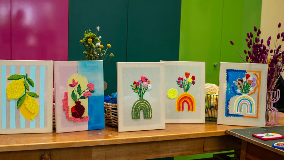 Bunte Punch-Needle-Kunstwerke auf Holztisch.