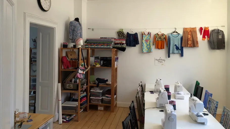 Nähzimmer mit Maschinen und aufgehängter Kleidung.