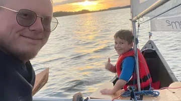 Mann und Kind segeln bei Sonnenuntergang.