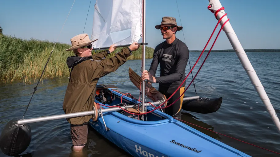 Two people setting up a sail on kayak.