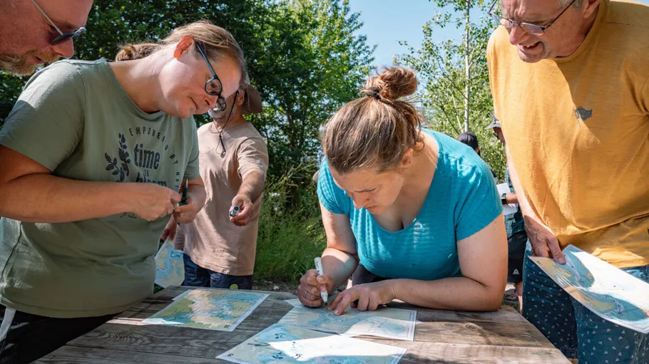 Personen studieren Karten an einem Holztisch im Freien.