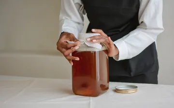 Person covering jar of kombucha on table.