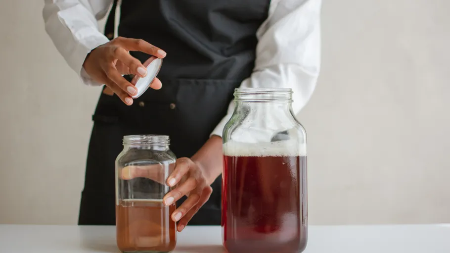 Person sealing jar with beverage on table.