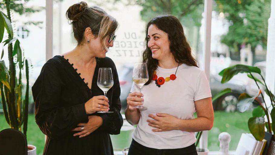 Two women smiling, holding wine glasses indoors.