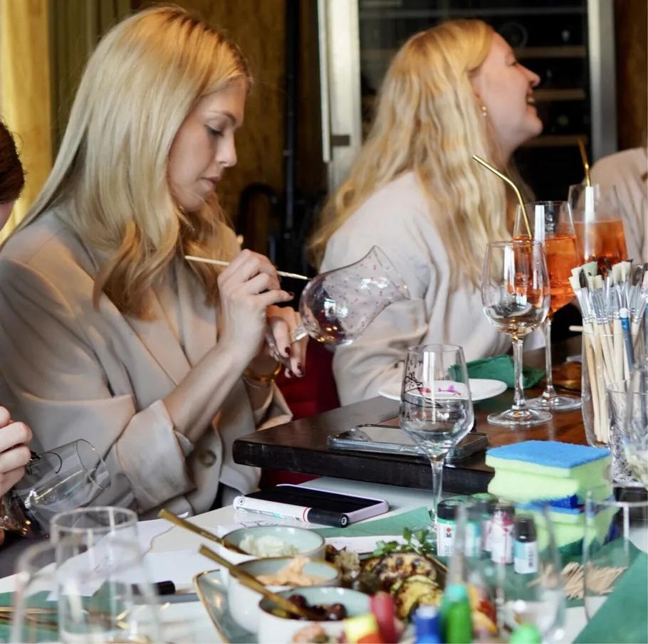 Zwei Frauen bemalen Weingläser am Tisch.