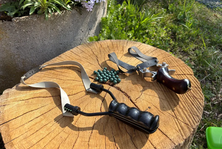 Two slingshots and ammo on tree stump.