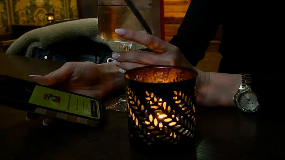 Hand holding drink, phone, candle lit table.