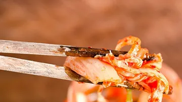 Essstäbchen halten Kimchi über einem Glas im Hintergrund.