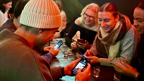 Group laughing at bar, checking phones.