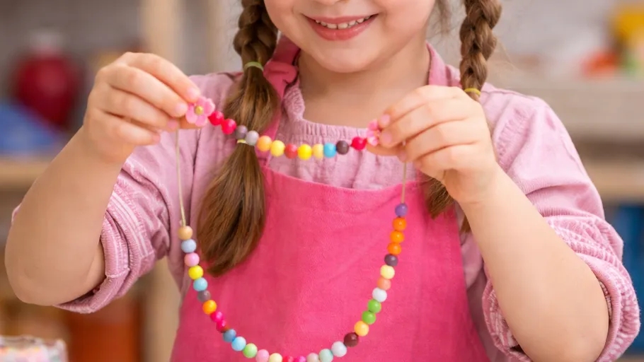 Young girl holds colorful bead necklace smiling.