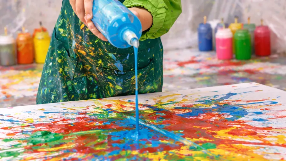 Person pouring blue paint on colorful canvas.