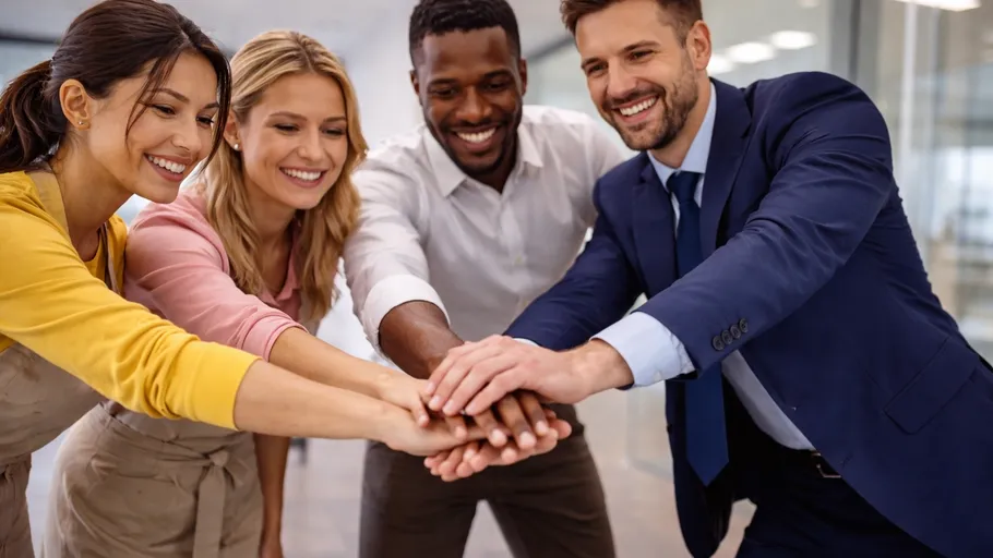 Group of colleagues stacking hands indoors.