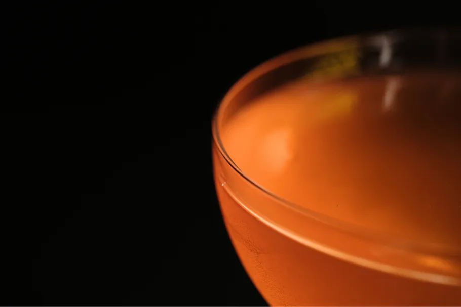 Orangenes Getränk in einem Glas vor schwarzem Hintergrund.
