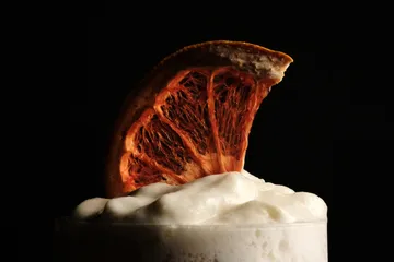 Getrocknete Orangenscheibe auf Schaum, dunkler Hintergrund.