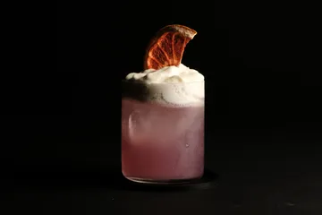 Purple cocktail with foam and orange slice.