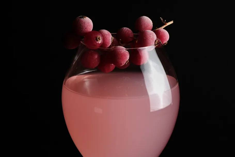 Pink drink in glass with grapes, dark background.