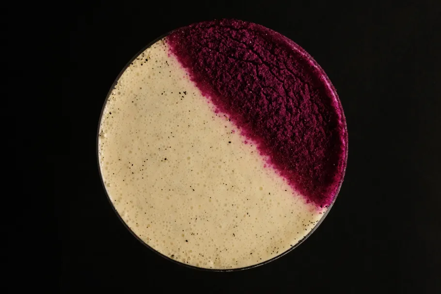 Coffee drink with purple garnish on black background.