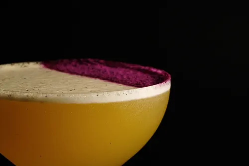 Gelber Cocktail mit lila Rand auf schwarzem Hintergrund.