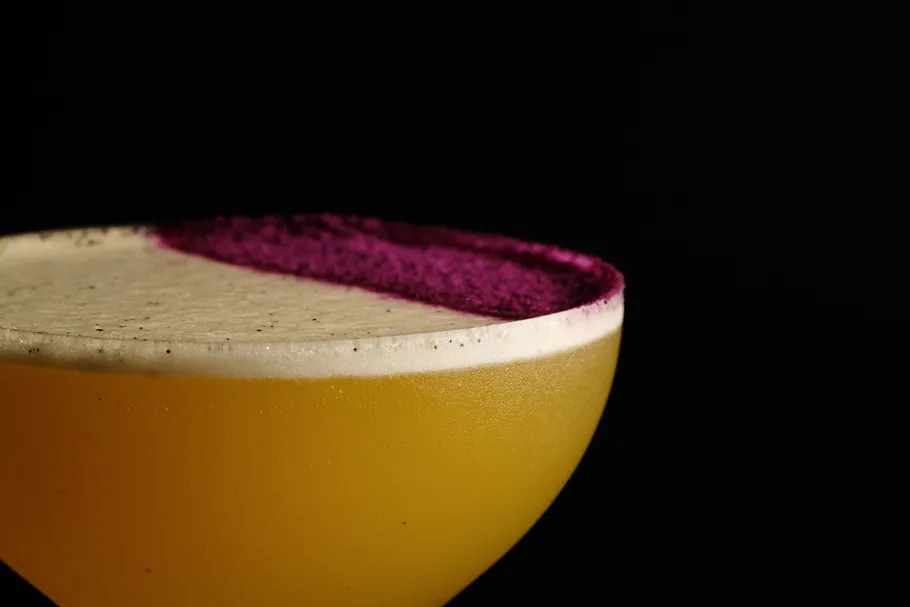 Gelber Cocktail mit lila Rand auf schwarzem Hintergrund.