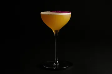 Gelber Cocktail im Glas vor schwarzem Hintergrund.