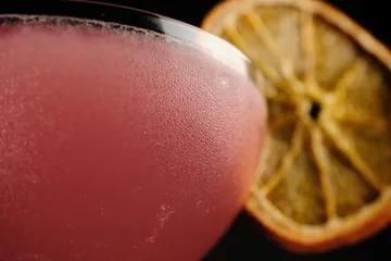 Pink cocktail with dried citrus garnish.